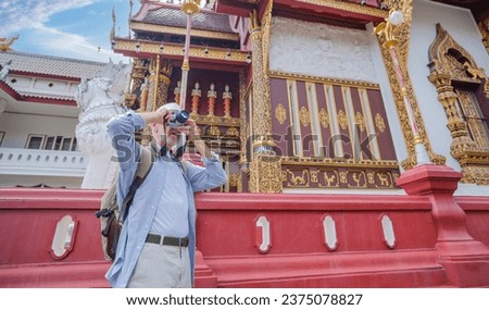 Elder Caucasian man visiting and admiring and taking pictures with his camera in beautiful Thai temple. he likes sun and travel. jorney concept.