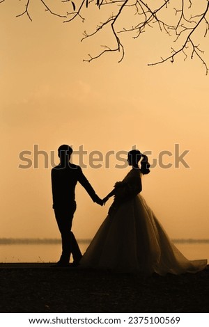 couple silhouettes holding hands and walking together looking each other in a date at sunset on the beach