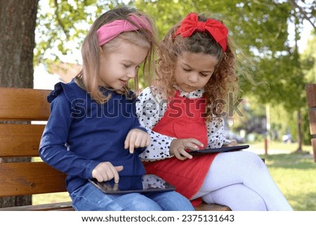 Two little girls are holding a tablet on the playground.using modern gadgets to watch videos and play games