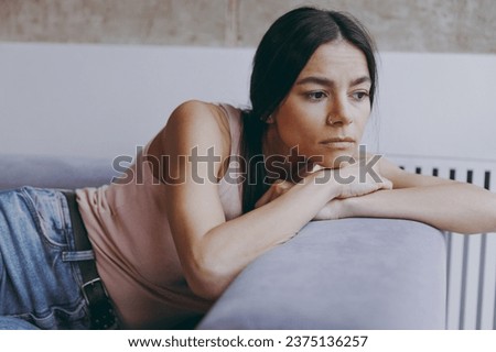 Unnerved sad worried minded young latin woman 20s in casual clothes sit lay on sofa think plan hands folded under head look aside spend time in living room home in own house. People emotions concept Royalty-Free Stock Photo #2375136257