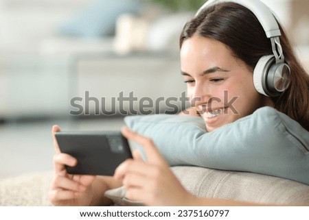 Happy woman wearing headphone watching media on smart phone at home
