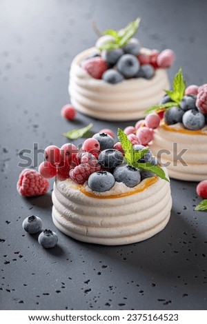 Creamy mini Pavlova dessert with frozen fruit and whipped cream. Pavlova dessert with frozen blueberries and raspberries. Royalty-Free Stock Photo #2375164523