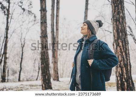 A young mature woman breathes fresh air and enjoys the snowfall in the winter forest. Winter walks and activity concept Royalty-Free Stock Photo #2375173689