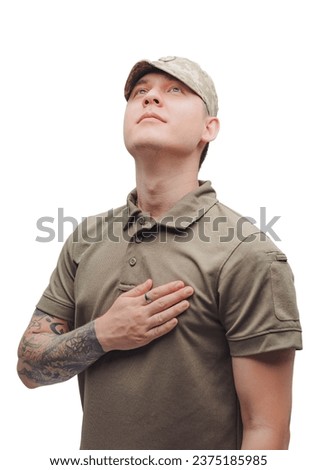 Portrait of a courageous Ukrainian military man isolated on white background, freedom concept. A young man with tattoos holds his hand over his heart.
