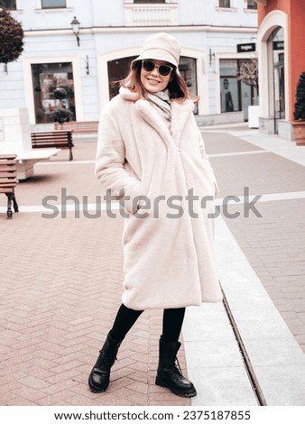 Young beautiful smiling lady wearing trendy white faux fur coat. Stylish woman posing in the street in winter. Cheerful and happy model in panama. Cold autumn weather. Shopping mall. In sunglasses