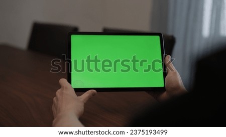 Man at home using tablet pc with green screen while sitting at the table