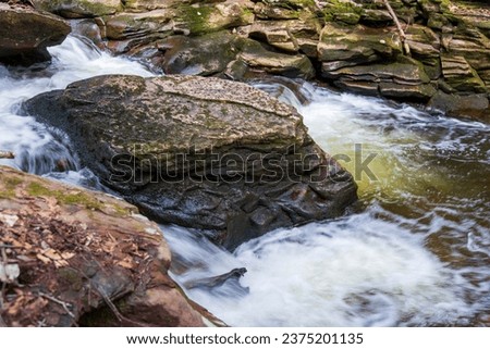 Rocky forest river in mountains. Slow shutter speed. Water waves and moss on stones