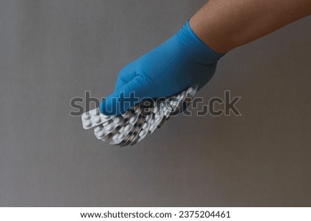 A hand in a blue medical glove holds blister packs of pills 