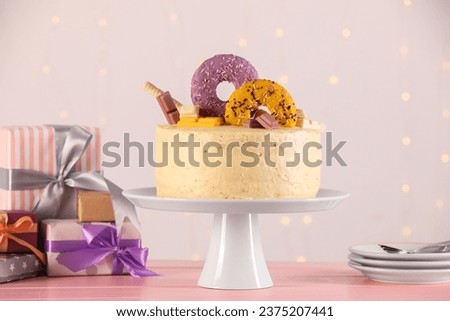 Delicious cake decorated with sweets, gift boxes, saucers and spoons on pink wooden table