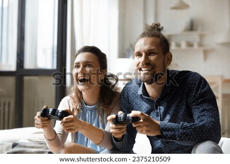 Cheerful excited young couple playing virtual video games, using controllers, console for VR fight, screaming, laughing enjoying home activity, leisure, indoor entertainment