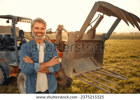 Mature handsome male farmer standing near a tractor on a field on a hot day and working on the farm. Agriculture and agriculture concept. Royalty-Free Stock Photo #2375215325