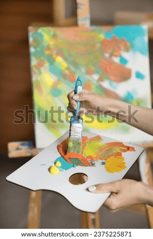 Vertical close up view unknown female hands hold palette and paintbrush, mixing acrylic paints colors drawing pictures, enjoy hobby or professional occupation alone in professional artistic workshop