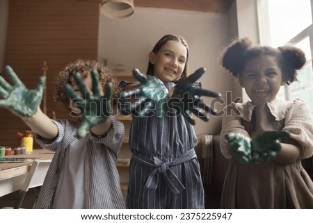 Happy kids showing painted palms smiling looking at camera. Playful three multiethnic little children showing their hands covered in paints, enjoy painting classes in art-studio. Fun, education, hobby Royalty-Free Stock Photo #2375225947