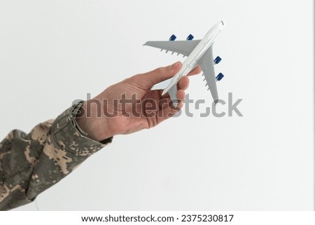 Military Technical Service, Air Force Concept. Hands of a man in uniform holding a silver toy airplane. A middle-aged adult man in a green camouflage uniform. Indoors. Selective Focus. Low key