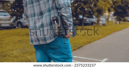 Close-up. Skateboard in a man's hand. A man carries a skateboard under his arm along a city street in autumn. A man likes to move quickly through city streets on a skateboard.
