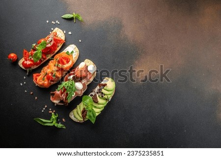 a set of bruschetta with prosciutto, salmon, tomatoes and avocado on a dark background. top view. place for text.