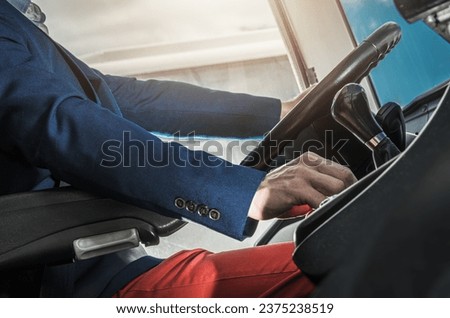 Driver Behind Large Coach Bus Steering Wheel Top View. Commercial Public Transportation. Transport Industry Theme. Royalty-Free Stock Photo #2375238519