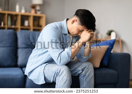 Depression Issue. Upset Korean guy crying resting head on fists, revealing sadness through his expression sitting at home, Moment of vulnerability and solitude, emotional distress concept Royalty-Free Stock Photo #2375251253