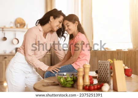 Mom and little daughter sharing heartfelt moment touching foreheads while preparing a healthy salad, cherishing family love and bonding during dinner preparation in kitchen at home Royalty-Free Stock Photo #2375251391