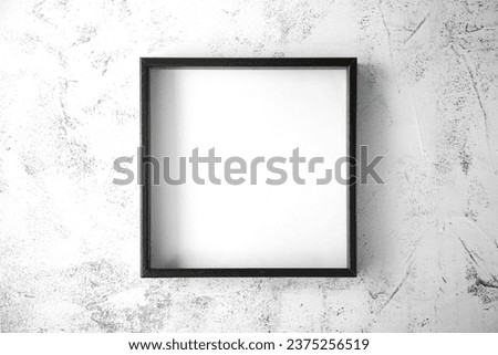 The black square frame is on a textured light with gray splashes  background in the center of the image. View from the top. Copy space.