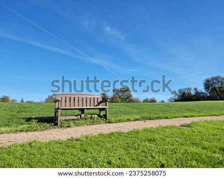 One simple bench on a beautiful sunny day with a clear sky and bright green grass.