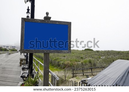 Blank blue sign on a wooden post on a gray wooden boardwalk on an overcast day
