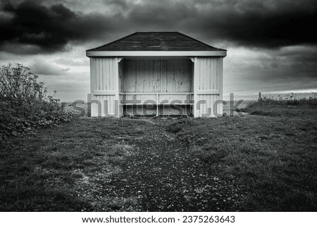 Gloomy and desperate image of an isolated timber beach hut and bench seen on a deserted beach, taken just before a heavy storm front. Royalty-Free Stock Photo #2375263643