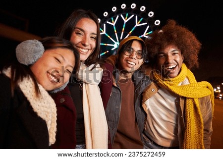 Portrait of group happy generation z people taking selfie mobile photo in winter night looking smiling at camera at amusement park . Young joyful multi-ethnic friends having fun together in community.