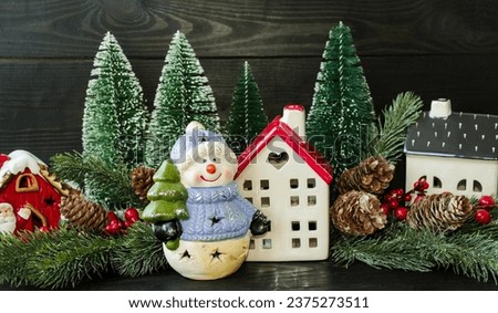 New Year's card, porcelain toy snowman with a Christmas tree in his hands and a New Year's forest house, green Christmas trees and a wooden sleigh.  Home decoration.  Background picture.