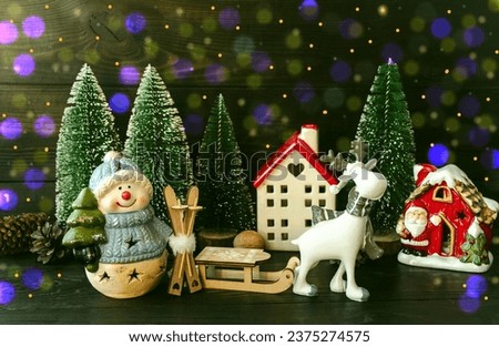 New Year's card, porcelain toy snowman with a Christmas tree in his hands and forest houses, white deer, green Christmas trees and wooden sleigh.  Home decoration.  Background picture.