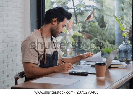 Attractive barista male or employee concentrate on stacks of tax declaration bills, restaurant owner using laptop for bookkeeping control payment, multitask small business lifestyle doing everything Royalty-Free Stock Photo #2375279405