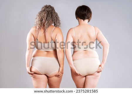 Two overweight women with fat flabby back, hips and buttocks on gray studio background, plastic surgery and body positive concept