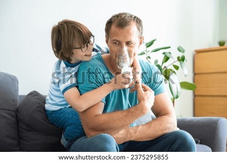 Happy child boy treats his dad at home. Medical procedures. Inhaler. Respiratory medicine. Home treatment Royalty-Free Stock Photo #2375295855