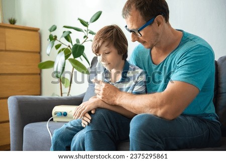 Father helps his child boy to makes inhalation at home. Young man with son doing inhalation with a nebulizer. Child, Ventilator, Breathing Exercise, Problems, Patient Royalty-Free Stock Photo #2375295861