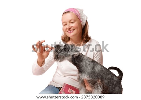 A woman feeds pieces of meat to dog, training obedience in eating, pink studio background, isolated on white background.