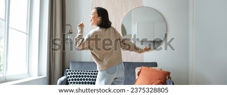 Beautiful asian woman dancing, feeling happy and upbeat, singing into hand microphone, express joy, positivity and happiness.