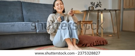 Portrait of young woman with remote, watching tv, switching chanels on television, sitting on floor near sofa and relaxing.