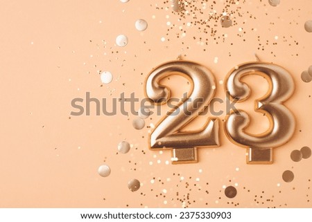 23 years celebration. Greeting banner. Gold candles in the form of number twenty three on peach background with confetti.