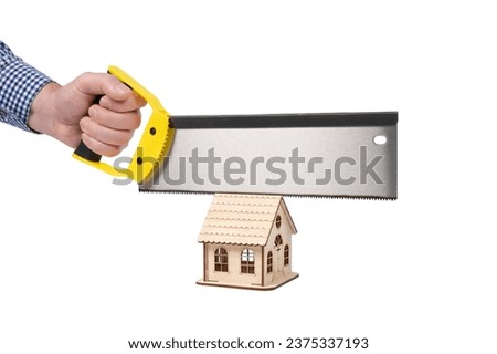A man's hand holds a saw for woodworking and cuts a wooden toy house. Conceptual image. Isolated on white background.
