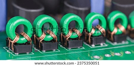 Row of toroidal transformer inductors on PCB for audio or video signal galvanic isolation. Closeup of electronic coils with copper wire on green ferrite core in black holders on printed circuit board. Royalty-Free Stock Photo #2375350051
