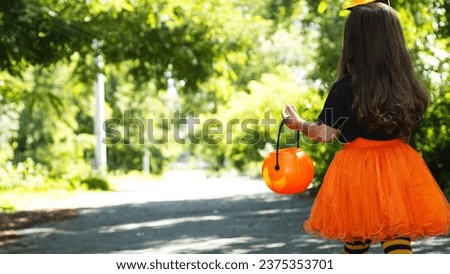 Copyspace background with child dressed in festive costume for Halloween trick or treating. kid in orange black striped stocking holding pumpkin basket, back view low section