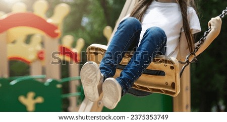 Little girl having fun on a swing on the playground in public park on autumn day. Happy child enjoy swinging. Active outdoors leisure for child. Royalty-Free Stock Photo #2375353749