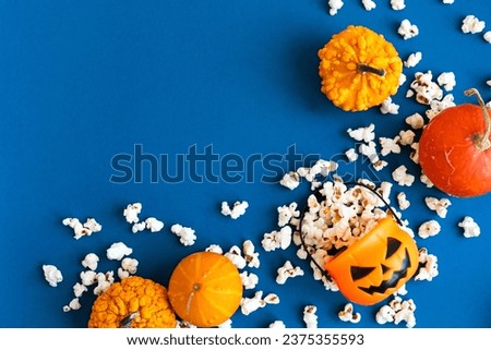 Jack o lantern basket full of popcorn and decorative pumpkins on a blue background with copy space. Movie night concept. Watching TV themed photo. Fall or autumn TV shows.