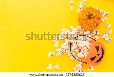 Jack o lantern basket full of popcorn and small decorative pumpkinson a yellow background with copy space. Halloween banner. Autumn or fall movie concept.  Movie night concept. Watching TV themed.