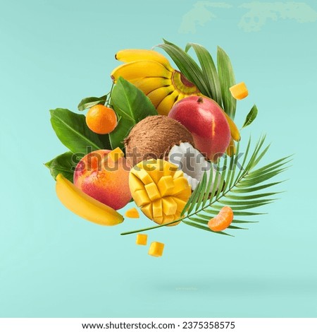 Exotic fruit mix, coconuts, mango, fig, passiflora, carambola falling in te air isolated on blue background. Food levitation, zero gravity conception. High resolution image