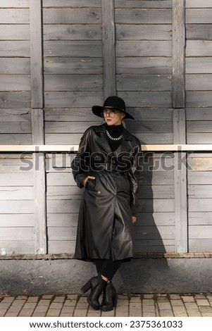 Portrait of an attractive and young blonde woman in a black hat and a leather trench coat while walking around the city. The concept of style and fashion.