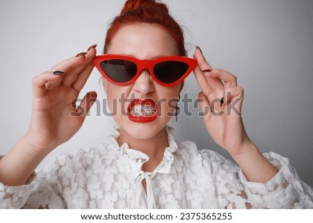 Portrait of angry young woman wearing cat-eye sunglasses posing on white background. 