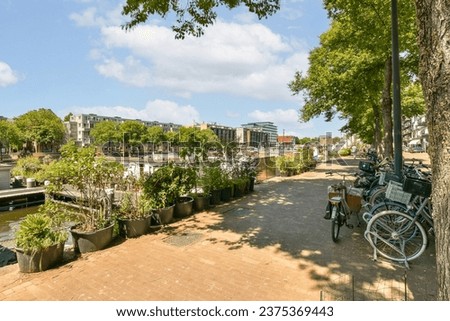 a bike parked next to a tree on the side of a river with buildings in the background and blue sky Royalty-Free Stock Photo #2375369443