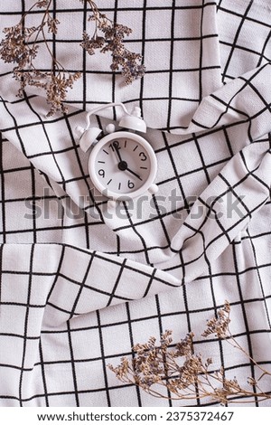 Change to winter time. Alarm clock and dried flowers on checkered crumpled fabric top and vertical view