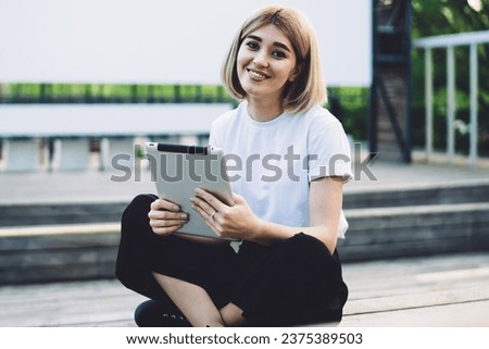 Pleased adult female surfing tablet sitting on stage in street